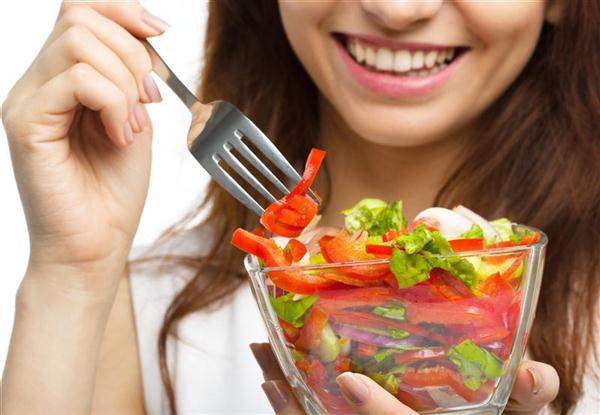 Young attractive woman eats vegetable salad using fork, isolated over white